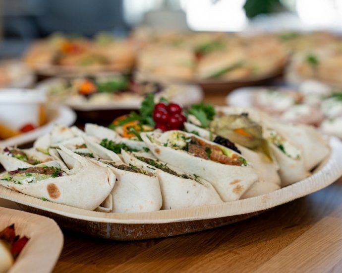 A wooden platter of assorted vegetarian wraps with fresh ingredients, perfect for parties.